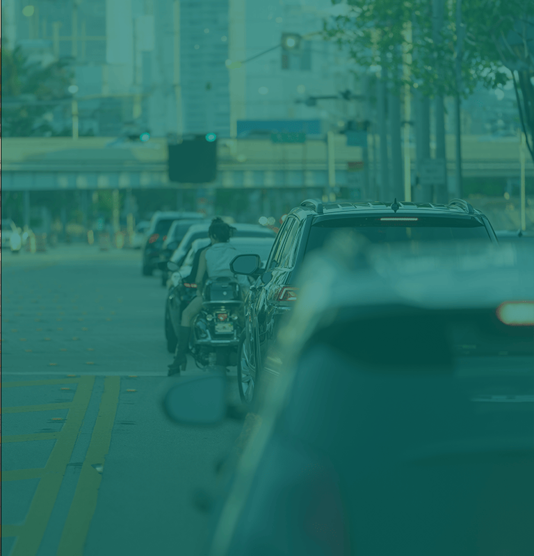 Vehicles in traffic on an urban roadway with a blurred city skyline in the background.