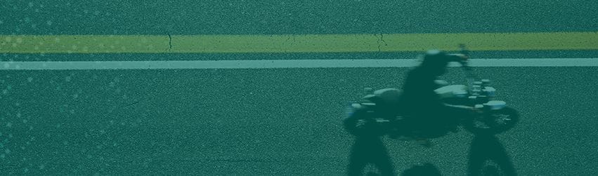 Silhouette of a motorcycle rider on a road with a yellow lane marking.